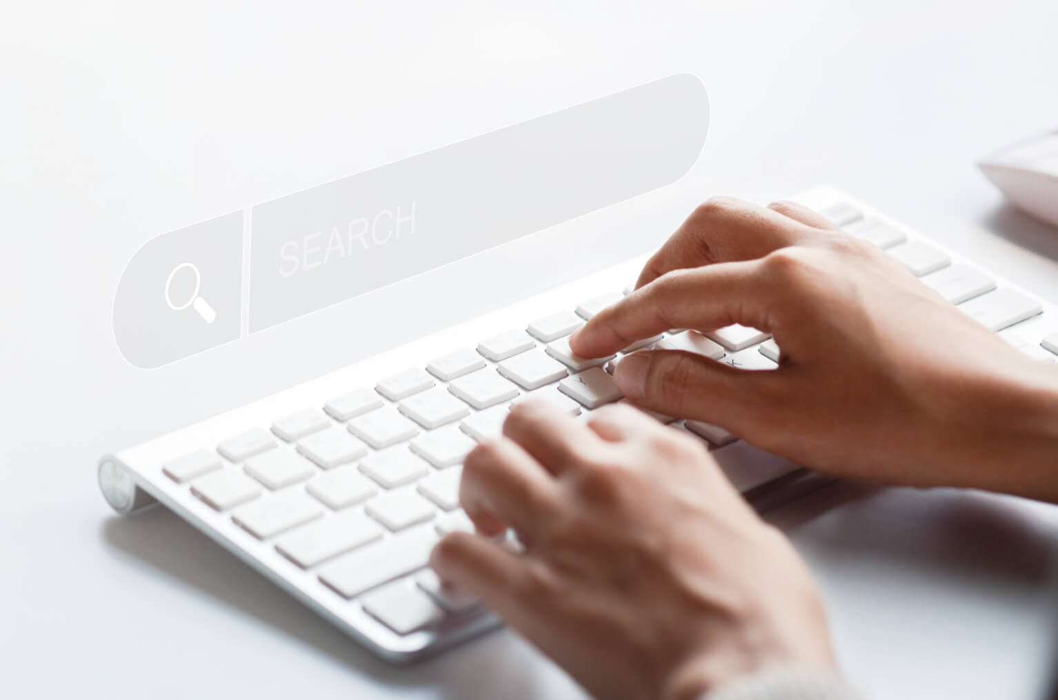 Close-up image of hands typing on a white keyboard with a search bar graphic to illustrate AI-powered search for websites.